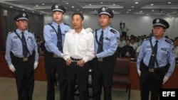 Bo Xilai, esposado, con los puños apretados en una aparente muestra de resistencia, rodeado por dos altos policías que lo sostenían de los hombros y antebrazos. 
