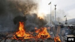 Manifestantes permanecen tras pilas de neumáticos incendiados durante las protestas violentas en el centro de Kiev (Ucrania), hoy, miércoles 19 de febrero de 2014.