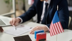 Foto: Envato (Web Screenshot) Close up of approved and rejected stamps on table in US immigration office with flag, copy space