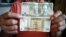 Un trabajador muestra un peso cubano (CUP) y un 1 CUC, que según la tasa oficial de cambio equivale a 25 CUP.